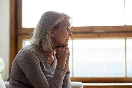 139912815-side-view-of-sad-thoughtful-middle-aged-mature-woman-sit-on-couch-at-home-look-in-window-distance-mo